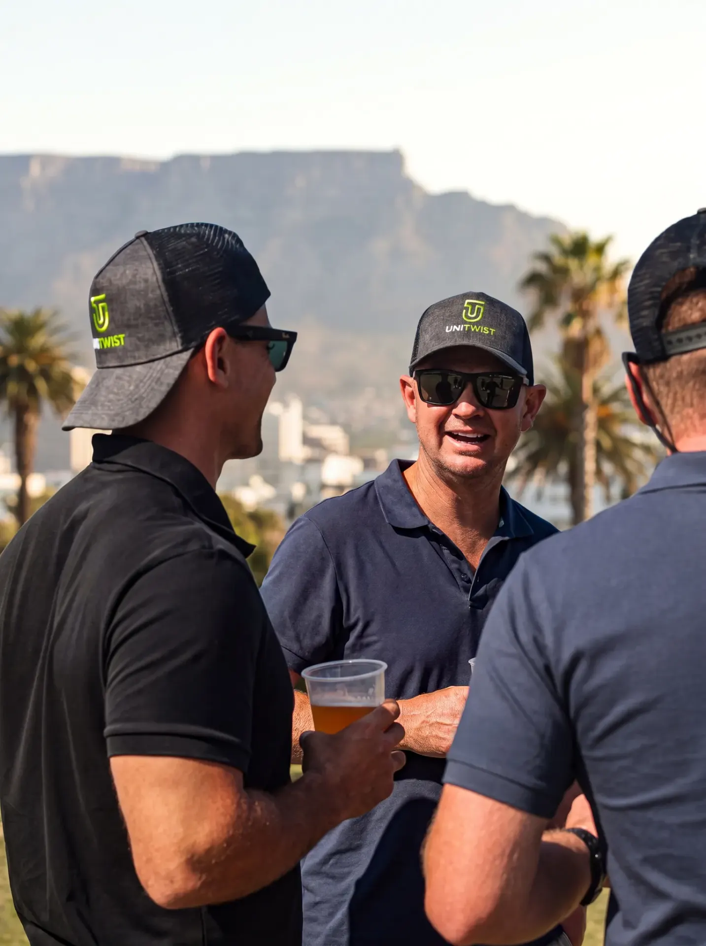 Unitwist Golf Day - three men standing with Unitwist caps on with table mountain in the background 